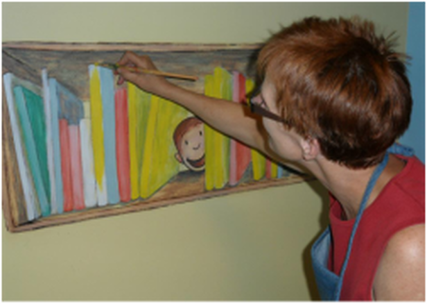 Debbie Wagner painting a mural of Curious George